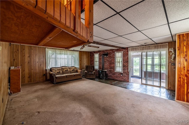 unfurnished living room with wood walls, brick wall, carpet flooring, and a wood stove