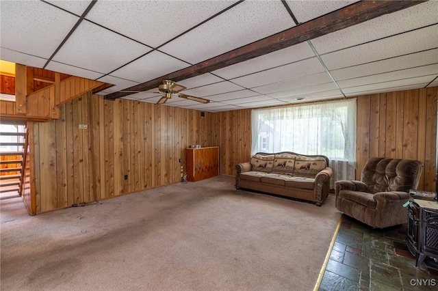 living room with dark colored carpet, ceiling fan, a paneled ceiling, and wooden walls