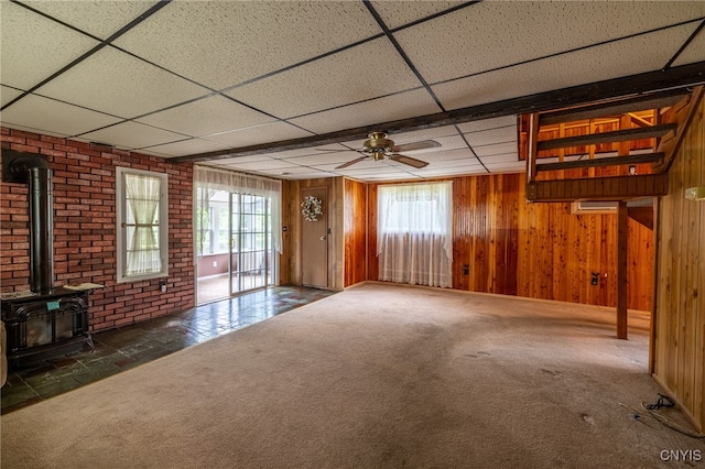 interior space featuring brick wall, a drop ceiling, a wood stove, and plenty of natural light