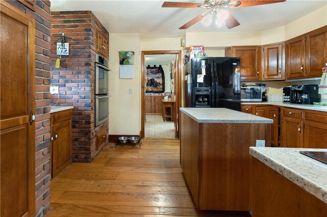 kitchen with appliances with stainless steel finishes, brick wall, ceiling fan, and light hardwood / wood-style floors