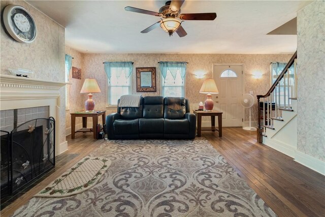 living room featuring wood-type flooring, a tiled fireplace, and ceiling fan