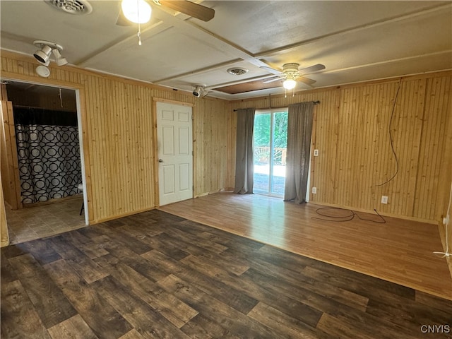 empty room with ceiling fan, wood-type flooring, and wooden walls