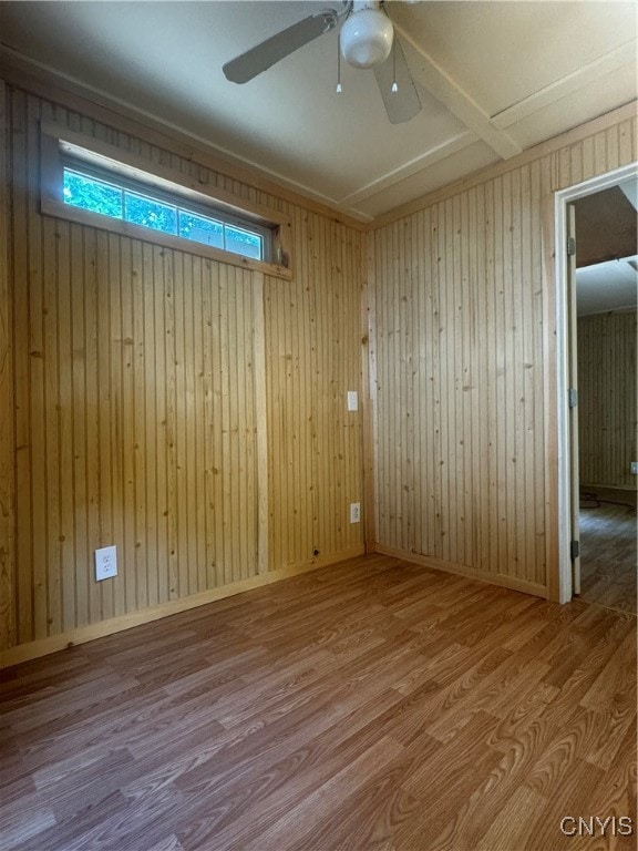 empty room featuring ceiling fan, wood walls, and hardwood / wood-style flooring