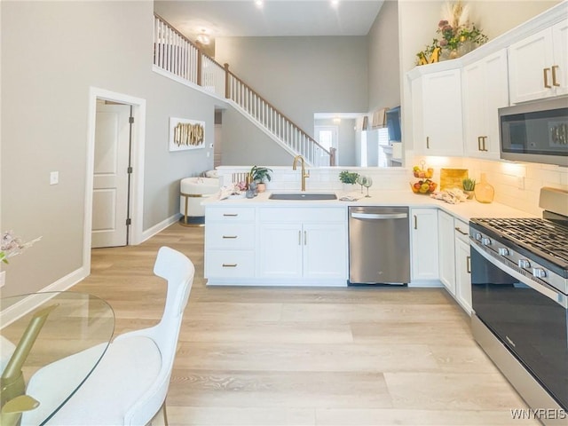 kitchen with light wood-style flooring, appliances with stainless steel finishes, white cabinetry, a sink, and a peninsula