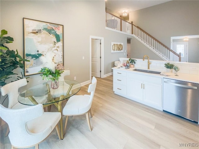 dining room featuring a towering ceiling, light wood-style flooring, baseboards, and stairs