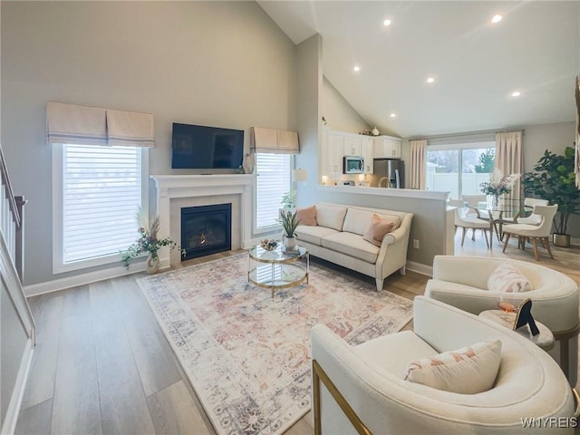 living room featuring a fireplace with flush hearth, recessed lighting, high vaulted ceiling, and light wood finished floors