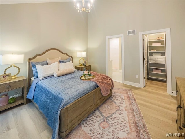 bedroom featuring connected bathroom, a high ceiling, a spacious closet, light hardwood / wood-style floors, and an inviting chandelier