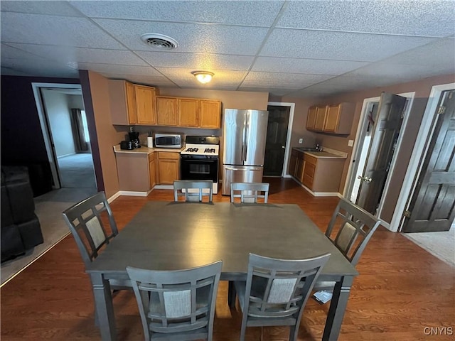 kitchen with a paneled ceiling, stainless steel appliances, wood finished floors, visible vents, and baseboards