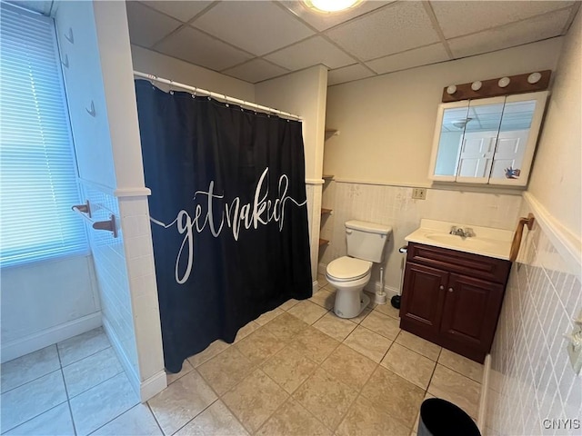 bathroom with a paneled ceiling, toilet, wainscoting, vanity, and tile patterned floors