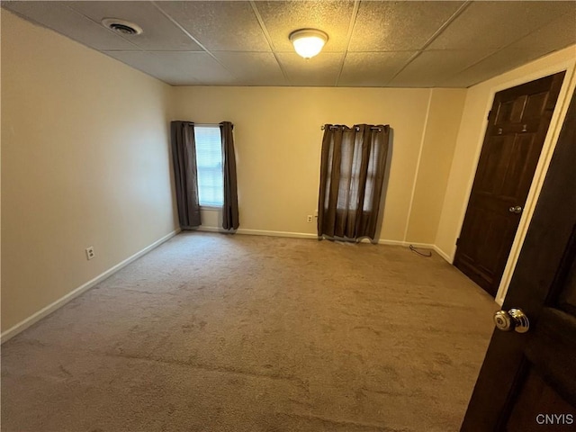 carpeted empty room with a paneled ceiling, visible vents, and baseboards