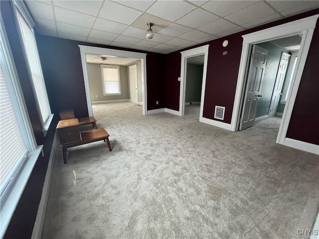 interior space featuring light carpet, baseboards, and a drop ceiling