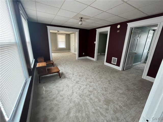 carpeted empty room featuring baseboards and a drop ceiling