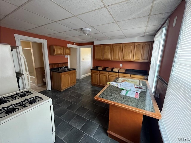 kitchen with white appliances, brown cabinets, a paneled ceiling, built in desk, and a sink