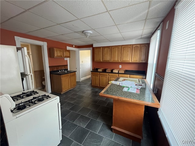 kitchen featuring dark tile patterned flooring, a center island, a paneled ceiling, white range with gas stovetop, and sink