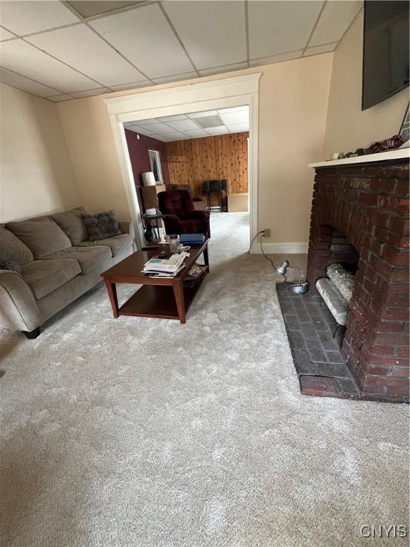 living room with a paneled ceiling, a brick fireplace, and carpet