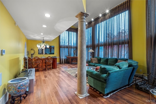 living room with ornate columns, wood-type flooring, indoor bar, and a notable chandelier