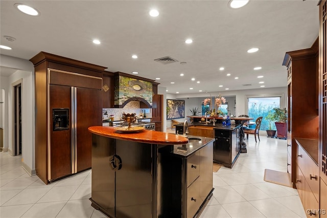 kitchen featuring a center island with sink, light tile patterned floors, paneled refrigerator, and sink