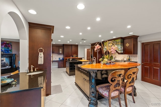 kitchen featuring tasteful backsplash, sink, light tile patterned flooring, and a center island with sink