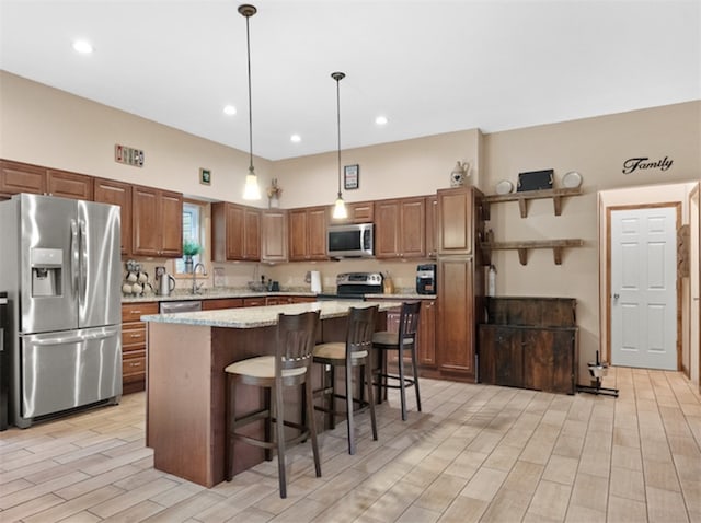 kitchen with hanging light fixtures, appliances with stainless steel finishes, light stone countertops, a kitchen breakfast bar, and a kitchen island