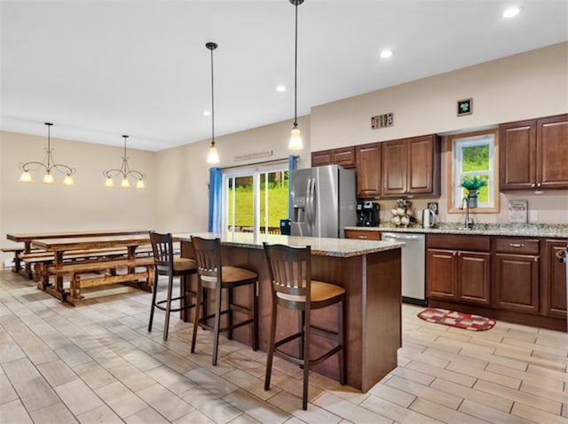 kitchen with stainless steel appliances, hanging light fixtures, light stone counters, a kitchen island, and a kitchen bar