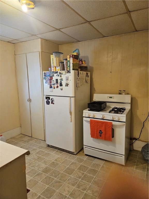 kitchen featuring white appliances, a drop ceiling, wooden walls, and light tile patterned floors