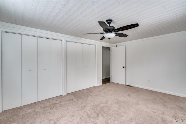 unfurnished bedroom with ceiling fan, two closets, and light colored carpet