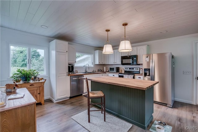 kitchen featuring stainless steel appliances, a center island, white cabinets, and decorative light fixtures