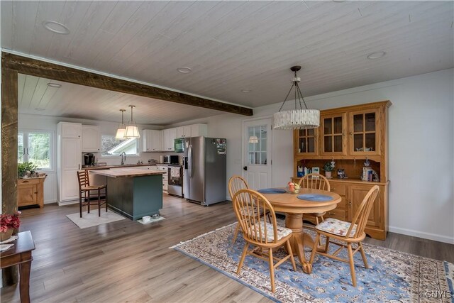 dining space with beamed ceiling, light wood-type flooring, and sink