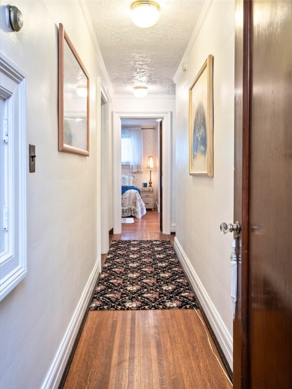 hall with wood-type flooring, a textured ceiling, and crown molding