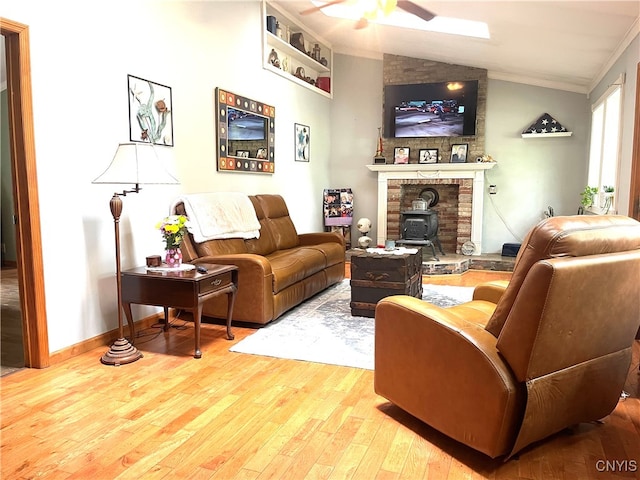 living room with light hardwood / wood-style flooring, a large fireplace, lofted ceiling, a wood stove, and ceiling fan