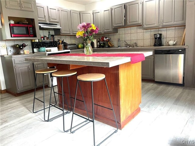 kitchen featuring a breakfast bar area, dishwasher, a center island, and gray cabinetry