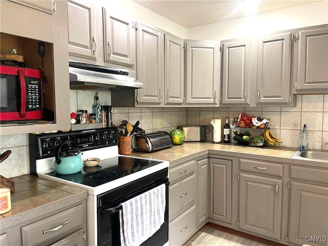 kitchen with electric range, gray cabinets, a sink, decorative backsplash, and under cabinet range hood