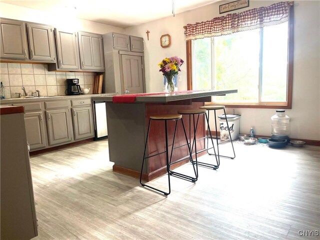 kitchen with gray cabinets, light wood-type flooring, tasteful backsplash, sink, and a breakfast bar area