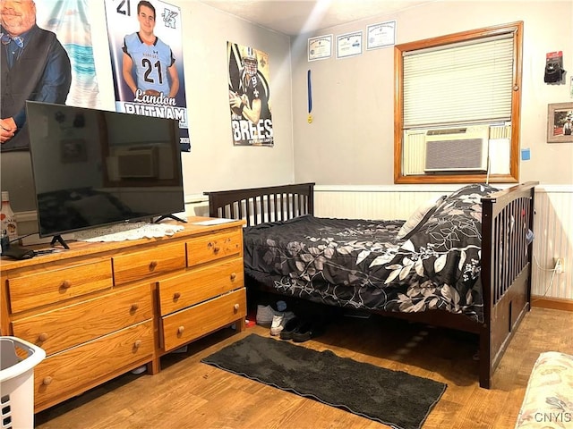 bedroom featuring cooling unit, wood finished floors, and a wainscoted wall