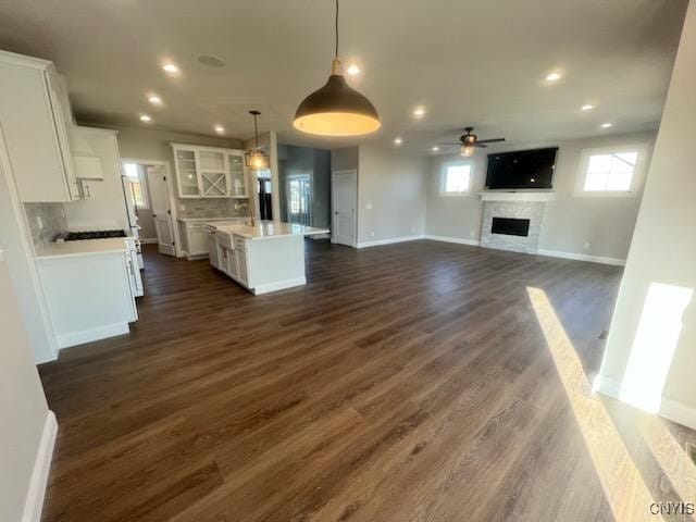 kitchen with dark wood-type flooring, an island with sink, white cabinetry, a fireplace, and light countertops