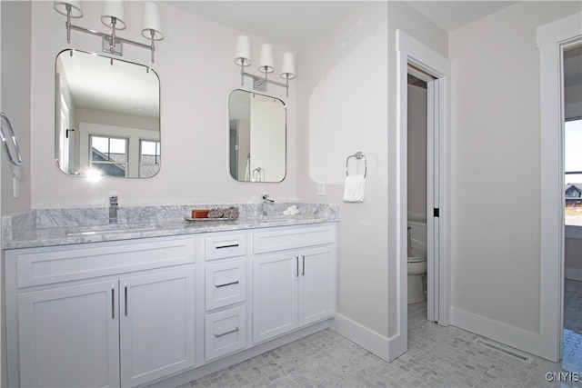 bathroom with double vanity, toilet, baseboards, and a sink