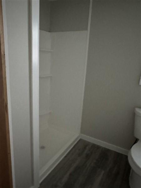 bathroom with hardwood / wood-style flooring, a shower, and toilet