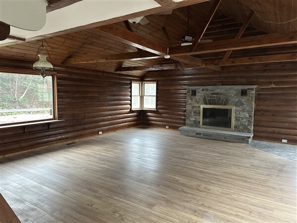 unfurnished living room featuring wood ceiling, hardwood / wood-style flooring, a stone fireplace, and lofted ceiling with beams