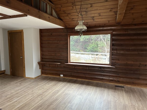 empty room featuring hardwood / wood-style floors, lofted ceiling with beams, wooden ceiling, and rustic walls