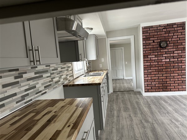 kitchen with gray cabinets, tasteful backsplash, butcher block counters, sink, and light hardwood / wood-style floors