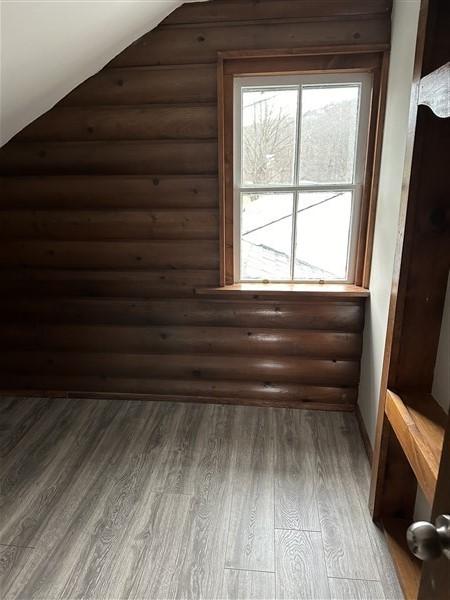 additional living space featuring lofted ceiling, hardwood / wood-style flooring, and rustic walls