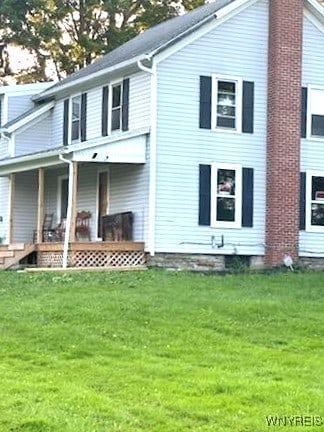 back of property featuring a lawn and covered porch