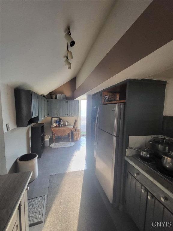 kitchen with concrete flooring, stainless steel refrigerator, and vaulted ceiling