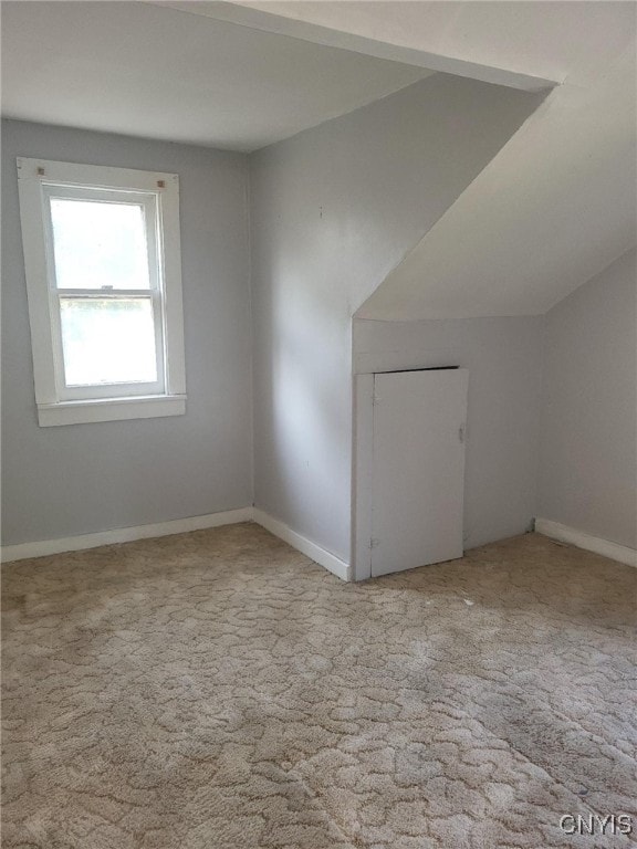 additional living space featuring vaulted ceiling and light colored carpet