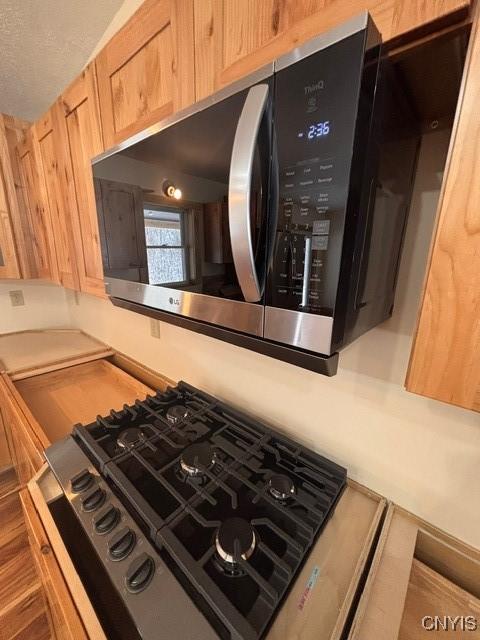 interior details with black gas cooktop, light brown cabinetry, stainless steel microwave, and light countertops