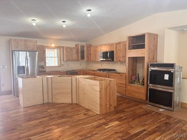 kitchen with lofted ceiling, appliances with stainless steel finishes, dark wood-type flooring, a center island, and light brown cabinets