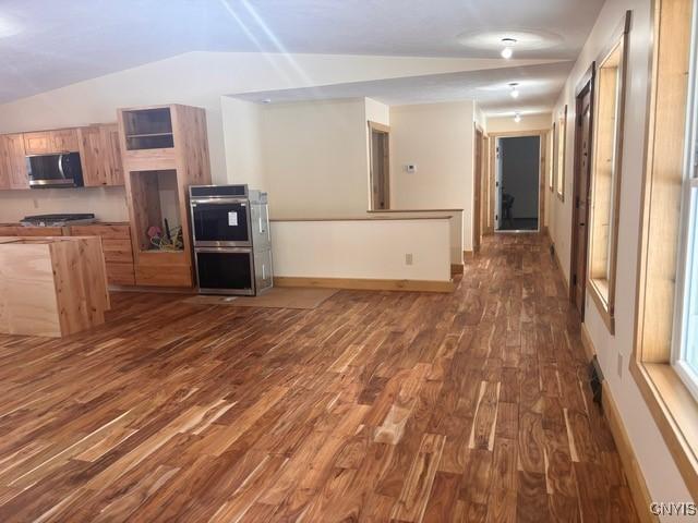 kitchen featuring dark wood finished floors, appliances with stainless steel finishes, open floor plan, vaulted ceiling, and baseboards