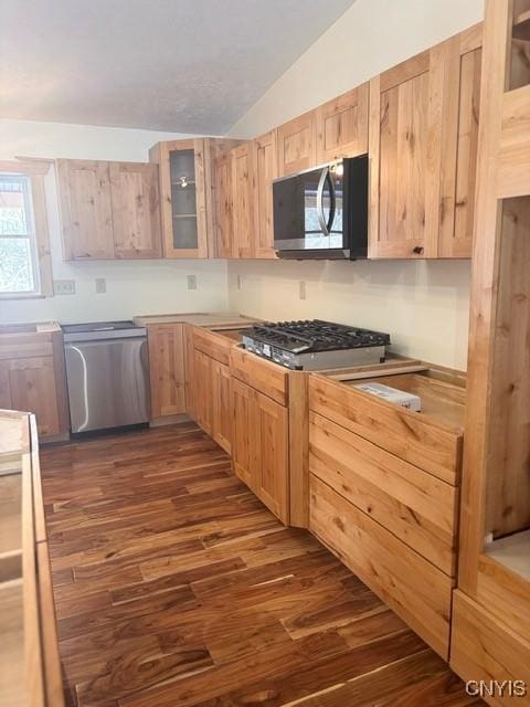 kitchen featuring glass insert cabinets, appliances with stainless steel finishes, dark wood-type flooring, vaulted ceiling, and light brown cabinets