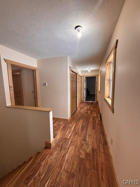 corridor featuring an upstairs landing, a textured ceiling, baseboards, and wood finished floors