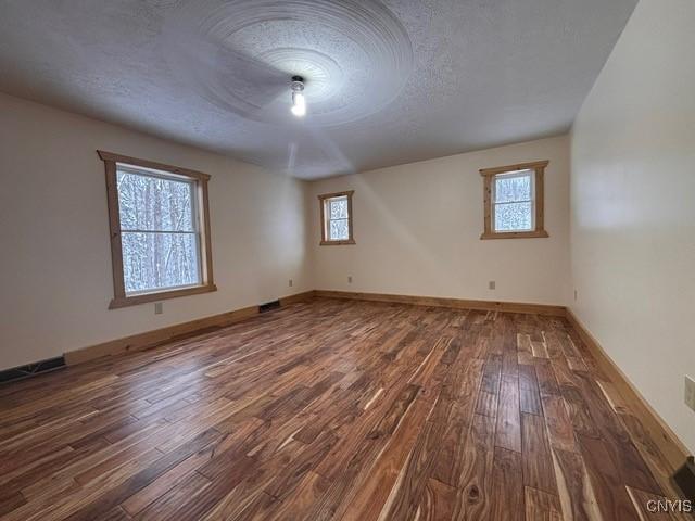 unfurnished room with a textured ceiling, baseboards, and wood finished floors